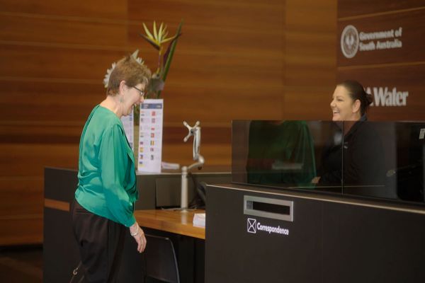 An older lady standing in front of a customer service desk in the SA Water building. A female SA Water staff member is sitting behind the desk, smiling back at the lady.